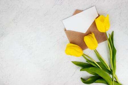 Colorful yellow tulips bouquet with envelope and letter flat lay on marble background top view with...