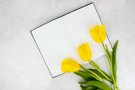 Colorful bouquet of yellow tulips and sketchbook, notebook flat lay on marble background top view...