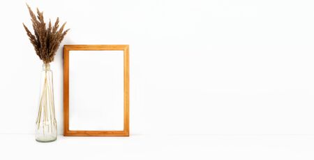 Wooden empty frame mockup with copy space, trendy dry flowers in glass bottle on white background....