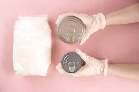 Sugar and female hands in gloves taking canned food flat lay on pink background. Quarantine isolation period food. Crisis food supplies. Delivery, donation, coronavirus, quarantine. Stock photo.の写真素材