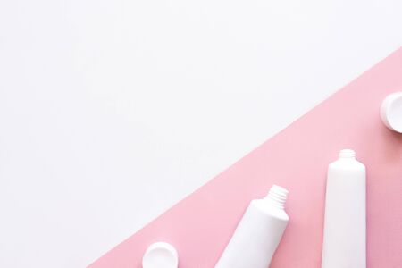 White squeeze tubes, bottles of moisturizing cream flat lay on pink and whiteの写真素材