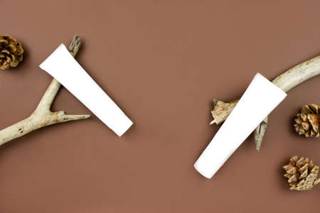 White squeeze tubes on wooden branches, bottles of cream flat lay on brown