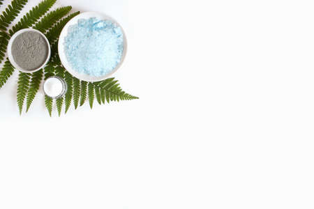 Sea salt, clay, cream, serum in brown dropper glass and spray bottle, green fern flat lay on white...