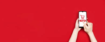 Female hands holding smartphone and press on shop now phrase, red background. Black friday and...