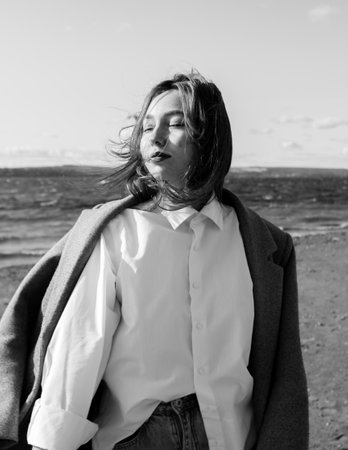 Portrait of a young woman in coat, white shirt and jeans with closed eyes enjoying of bright...