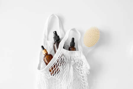 Serum, oil, acid, lotion in brown dropper glass with pipette, body brush in mesh bag flat lay on white. Spa products. Eco reusable shopping bag. Organic, natural cosmetic. Beauty, skincare. Zero wasteの写真素材