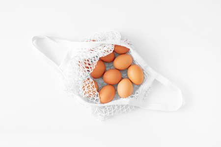 White mesh bag with brown eggs flat lay on white background top view copy space. Eco friendly,...