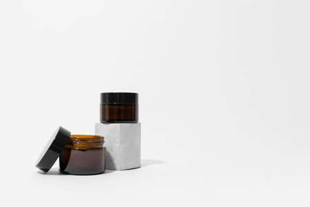Kit of brown glass jars with black caps on concrete pedestal white background, copy space. Cream ,serum, oil, lotion on podium. Zero waste glass. Organic, natural cosmetic. Beauty, skincare productの写真素材