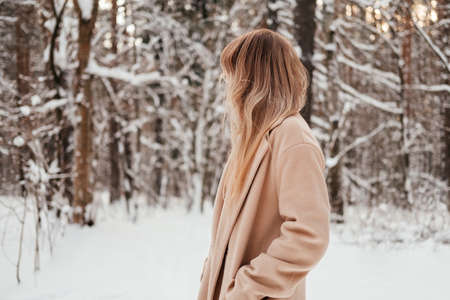 Unrecognizable woman in winter forest looking back. Girl with blonde hair in coat outdoors.の写真素材