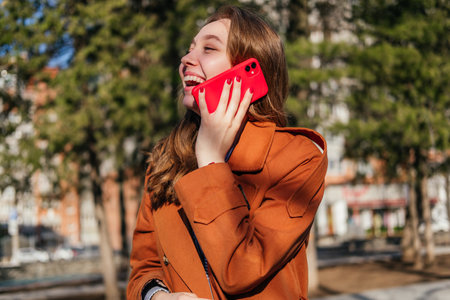 Laughing young woman talking on the phone outdoors. Girl having phone call on the street