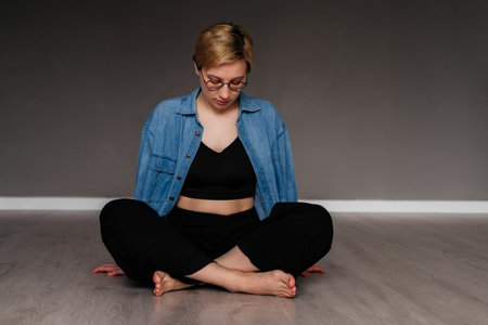 Young woman sitting in lotus pose on the floor meditating indoors. Girl doing yoga exercise in studioの写真素材