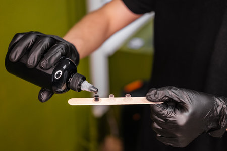 Male hands in gloves holding black ink. Tattoo artist preparing for work indoor. Small business and young professionals.の写真素材