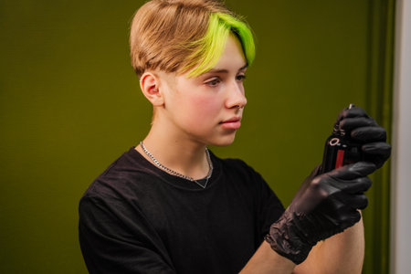 Young man tattoo artist with colored hair and piercing preparing for work indoor. Small business and young professionals.の写真素材