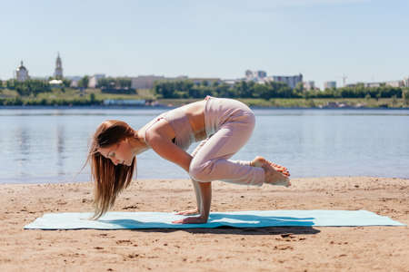 Middle aged woman in sportswear balancing on hands in bakasana yoga pose on sand. Stretching woman...