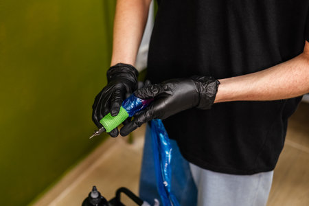 Male hands in gloves holding tattoo machine. Tattoo artist preparing for work indoor. young professionals.の写真素材