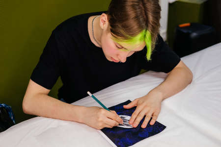 Young man tattoo artist with colored hair draws sketches indoor. Small business and young professionalsの写真素材