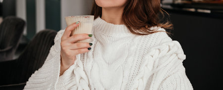 Young woman sitting at cafe and drinking coffee indoors. Caucasian girl in sweater.