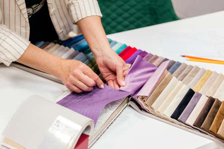Female hands choosing fabric for curtain indoor. Woman designer combining colors and textures in studioの写真素材