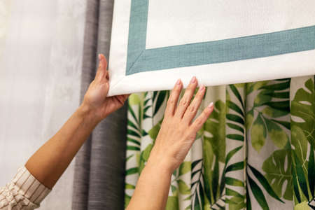 Female hands choosing fabric for curtain indoor. Woman designer combining colors and textures in...