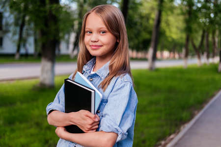 Smiling girl standing on street and holding notebooks. Child outdoor. Back to school conceptの写真素材