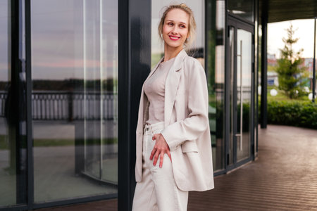 Smiling middle aged businesswoman in white clothes standing on street. Confident woman looking away outdoorの写真素材