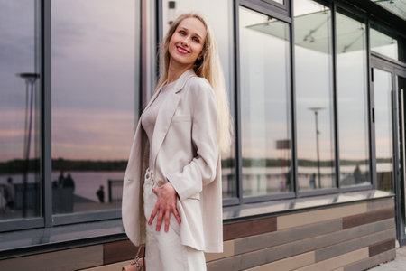 Smiling woman in white in white clothes standing on street near building outdoor. Businesswoman looking awayの写真素材