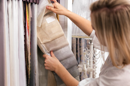 Woman choosing samples of fabric for curtain in textile store. Customer combining colors and textures indoorの写真素材