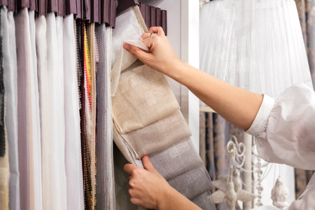 Female hands choosing fabric for curtain indoor. Customer in textile store. Woman designer combining colors and textures in studioの写真素材