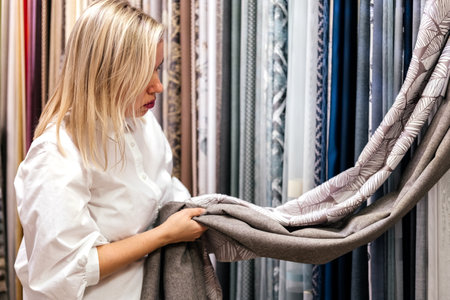 Woman in fabric store choosing and combining curtains indoor. Customer combining colors and textures in shopの写真素材