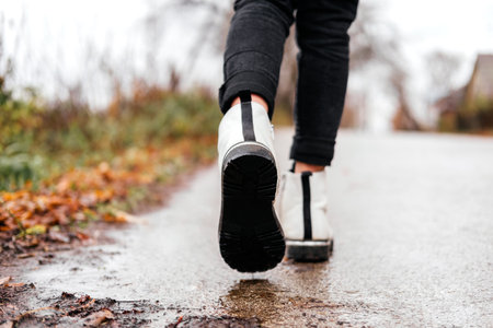 Unrecognizable kid walking in white boots on the road at autumn city street. Legs going forward outdoorsの写真素材