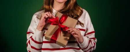 Unrecognizable woman holding gift isolated on green background. Female hands opening new year present. Holidays and christmas celebration conceptの写真素材