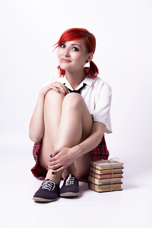 Red-haired girl, image in the style of anime, cheerful face, non-standard, piercings on his face, blue eyes, earrings tunnels, stack of books, tie and white shirt, photo in bright colors.の写真素材