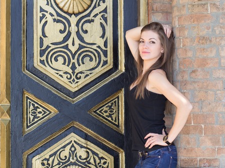 Portrait of a young girl, the girl on a walk around town, everyday makeup, wooden door with gold decoration, long hair, brick wall, jewelry made of gold.の写真素材