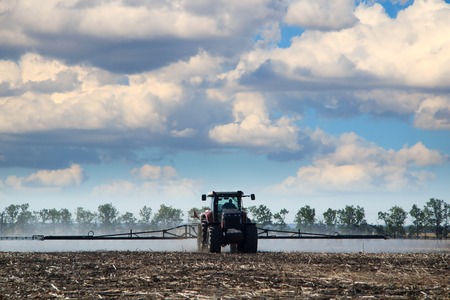 Tractor watering crops, the farmer drives a tractor, a tractor working in a field, agricultural machinery in operation, the machine sprays the groundの写真素材