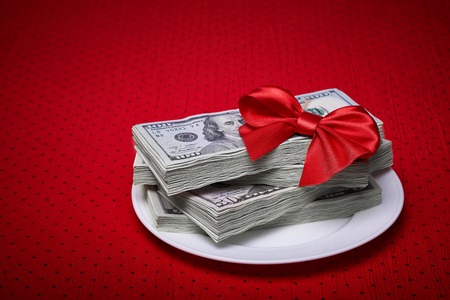 Bundle of dollars on a plate, paper money, red bow of the braid, economic concept, serving business lunch, a red tablecloth in a black polka dots.の写真素材