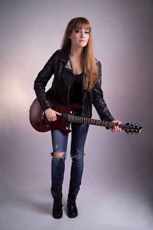 Girl with a guitar, leather jacket, bright makeup, electric guitar mahogany, standing with his guitar, vertical composition, stringed musical instrument, female feet.の写真素材