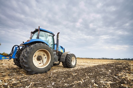 Tractor working in a field, agricultural machinery in the work, tractor in the background cloudy sky