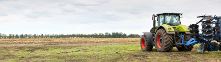 Tractor working on the farm, a modern agricultural transport, cultivation of fertile land, tractor on cloudy sky background, agricultural machineの写真素材