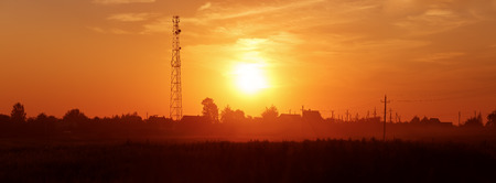 Sunset in the countryside. Silhouettes of houses, trees and power lines.の写真素材
