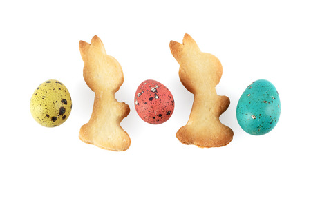 Multicolored painted quail eggs and biscuits in the shape of rabbits on a white background. 