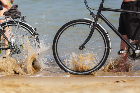 Sea wave splashing on the wheels of two bikes on the beach. Shallow depth of field.の写真素材