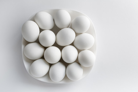 White eggs on a white square plate on a light background. Space for text. Top view.の写真素材