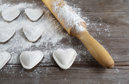 Raw heart shaped dumplings, flour and rolling pin on wooden background. Cooking ravioli. Shallow depth of field.の写真素材