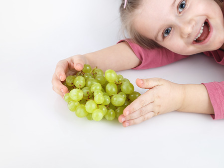 Happy child holding a bunch of ripe tasty sweet green grapes. Shallow depth of field. Focus on the bunch. Studio shot.の写真素材