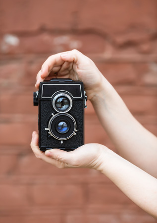 Retro vintage camera in female hands. Old brown vintage grunge wall in the  bokeh. Shallow depth of field. Selective focus on camera.の写真素材