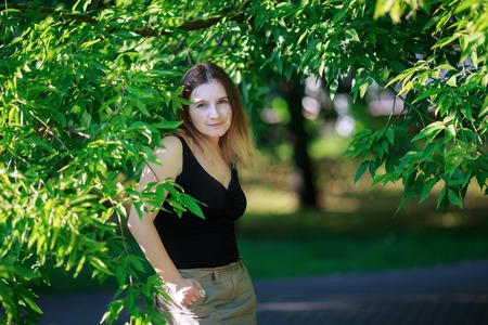 Girl posing in a park on a background of bright green foliage. Sunny summer day. Shallow depth of field. Selective focus on model.の写真素材