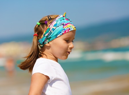 Profile of baby girl with a bandanna on his head on a blurred background of blue sky and sea. Hot sunny summer day. Selective focus.の写真素材