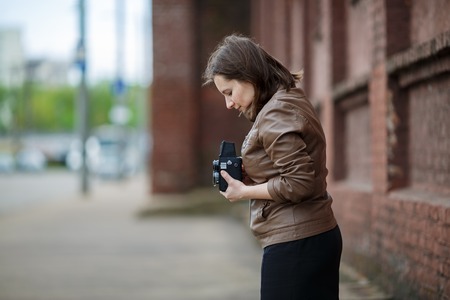 Female photographer taking photos in the street.  Woman with an old vintage camera outdoor. Shallow depth of field. Selective focus on model.の写真素材