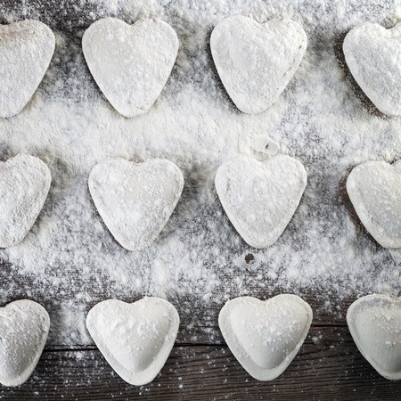 Cooking ravioli. Heart shaped dumplings, flour and rolling pin on wooden background. Top view.の写真素材