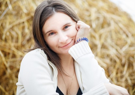Close-up outdoor portrait of a pretty young woman against blurred haystacks background.の写真素材